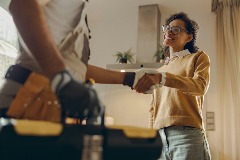 Close up of male handyman shaking hands with happy female client while standing at home kitchen