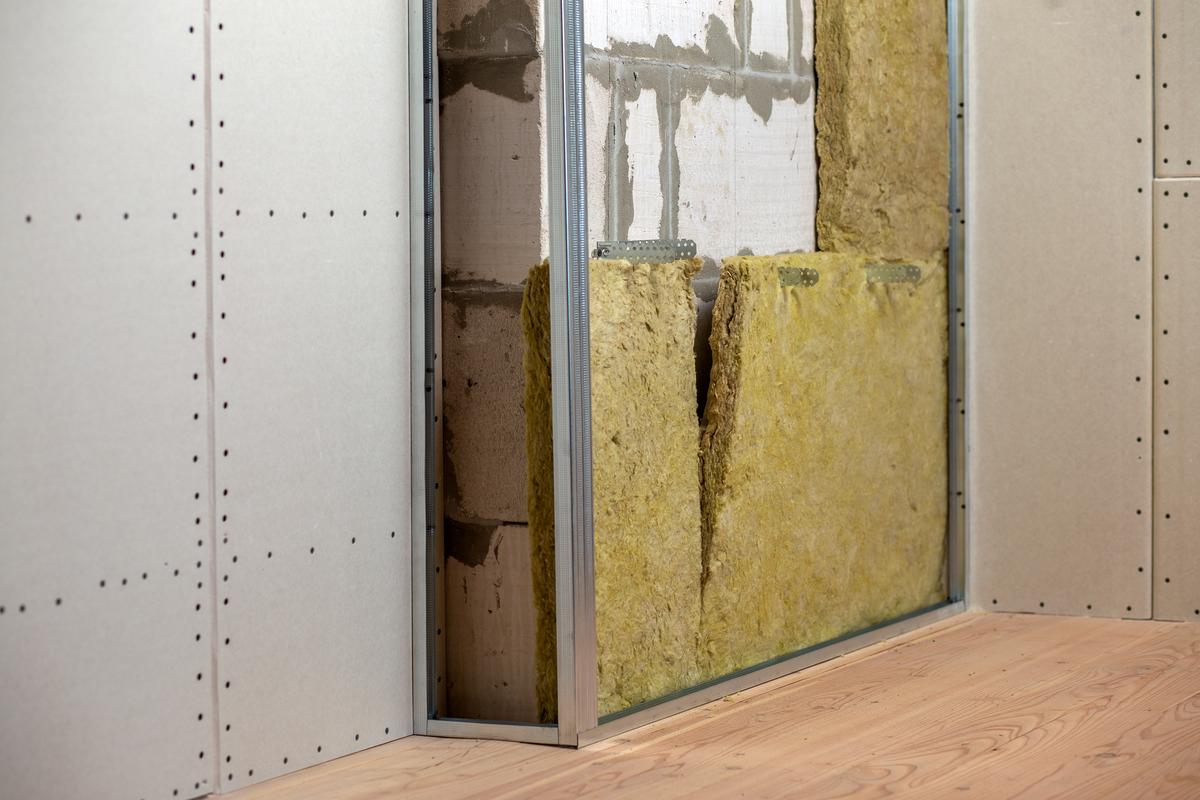 Wall of a room under renovation with mineral rock wool insulation and metal frame prepared for drywall plates.